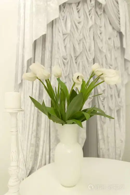 一束白色的郁金香在桌子上的花瓶在窗帘的背景上