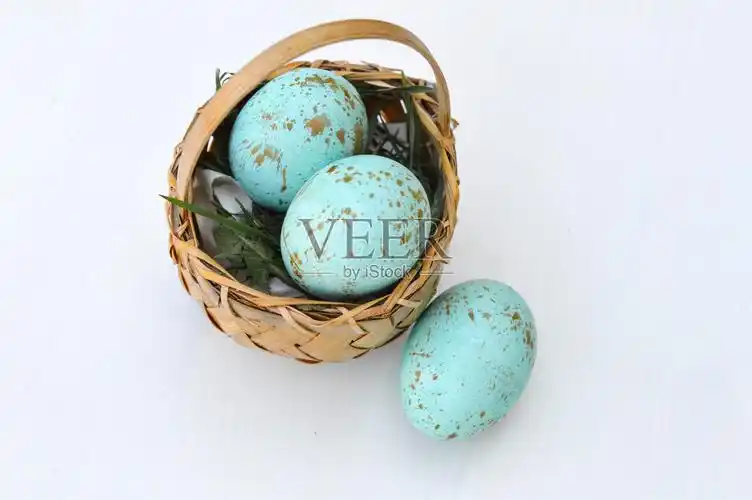 彩色的知更鸟蛋在一个小柳条篮子在一个白色的表面照片摄影图片