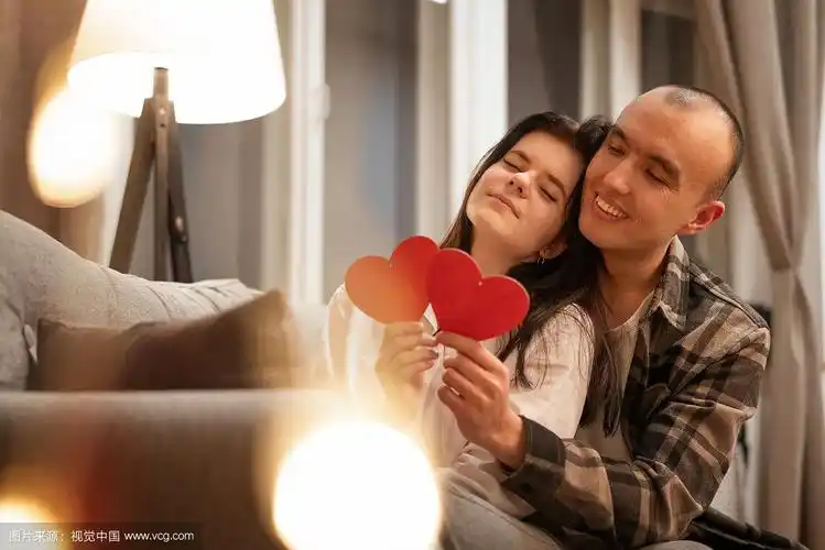 一对幸福的情侣坐在沙发上,怀里抱着一颗红心.漂亮的焦外成像模糊.