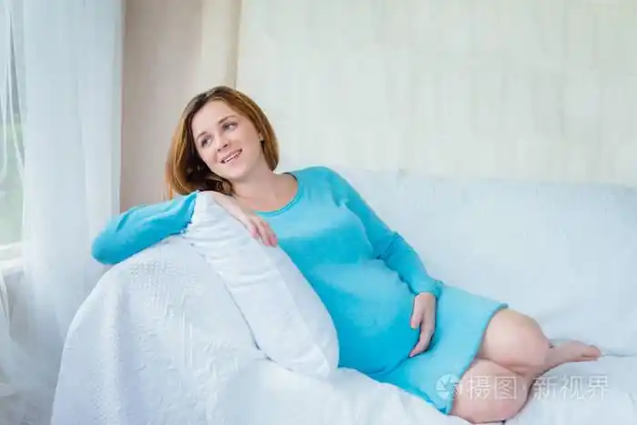 幸福的年轻孕妇躺在沙发上抱着肚子