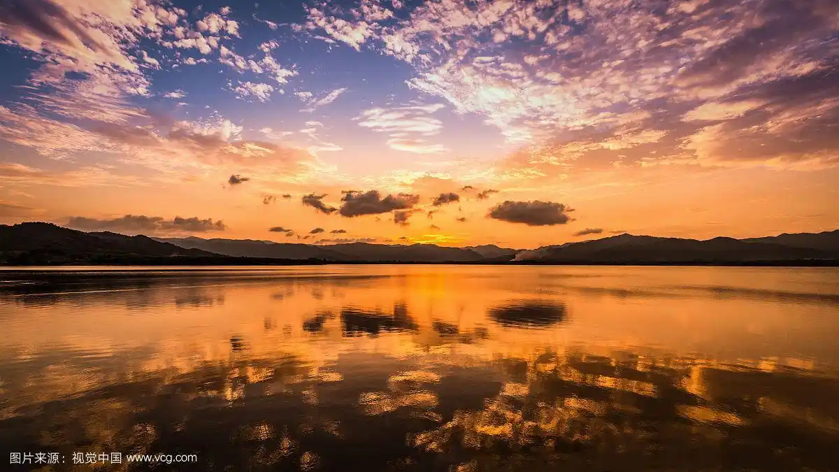 甜美的黄昏日落天空和云朵反射在平坦的水面上
