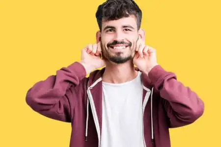 年轻的帅哥在孤立的背景上微笑着用手指有趣的手势拉着耳朵.