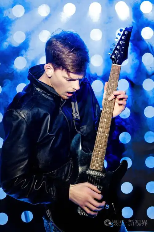 年轻有魅力摇滚音乐家弹电吉他和唱歌.对背景的聚光灯的摇滚明星