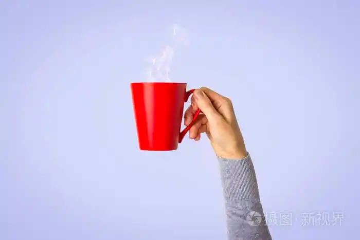 女性手拿着一个红色的杯子在浅蓝色的背景上放着热咖啡或茶早餐概念与