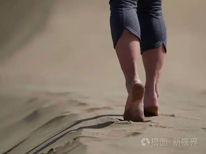 年轻女子跑步步行在日出海滩上赤裸的双脚