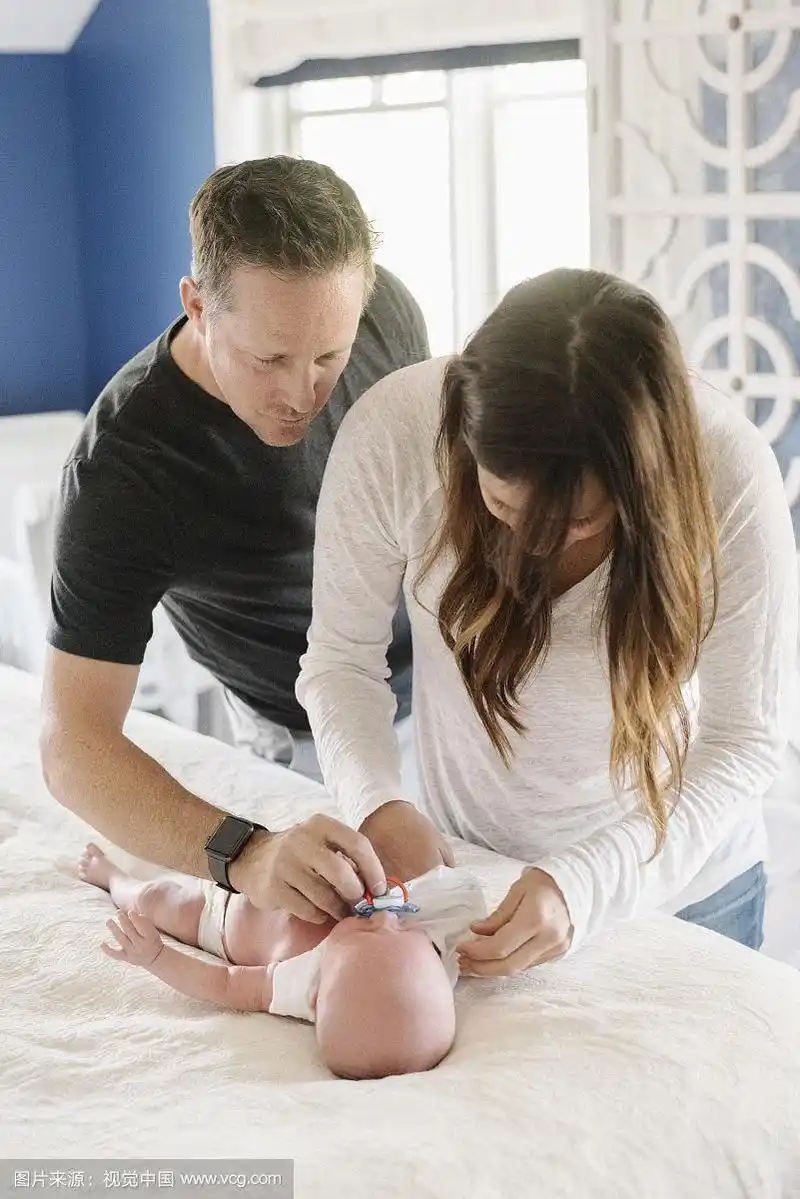 父母俩,妈妈和爸爸在换尿布台上,给婴儿换尿布.