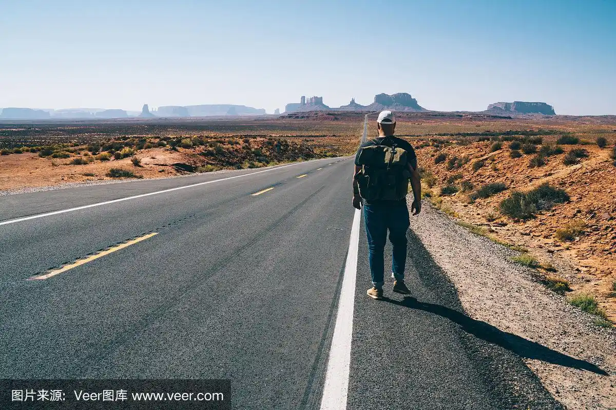 在美国西南部国家公园的柏油路上背着背包的男人的背影