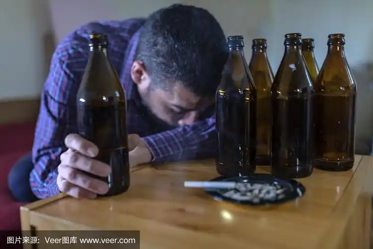 年轻悲伤的醉酒男子喝啤酒和酒精感到浪费,孤独和绝望