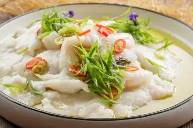 木质底纹上的圆瓷盘装的酸汤龙利鱼片