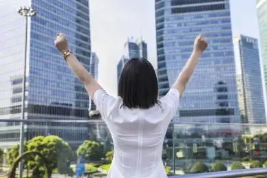 站在中央商务区户外高举双手的女商人背影,商务成功概念