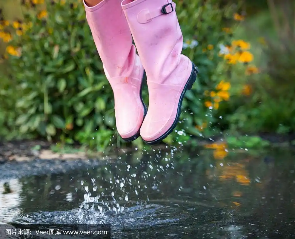 穿着粉红色雨靴的年轻女子在水坑里溅起水花