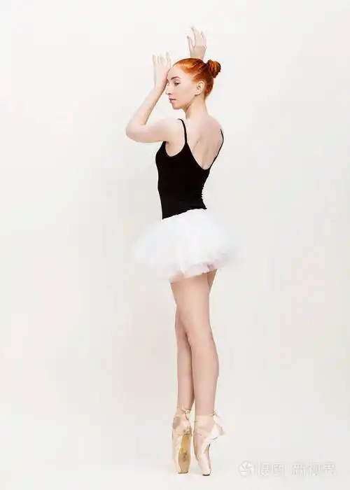 这位年轻美丽的芭蕾舞演员在一间光线充足的浅灰色工作室里摆姿势跳舞