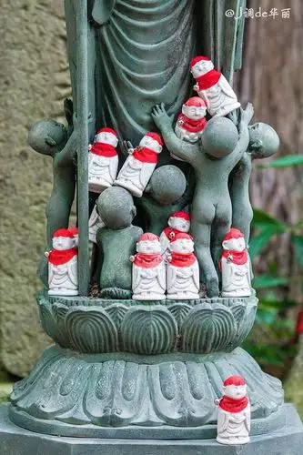 很多白色的瓷娃娃,脖子挂着铃铛和红色的围布,上面写着"水子地藏さん"