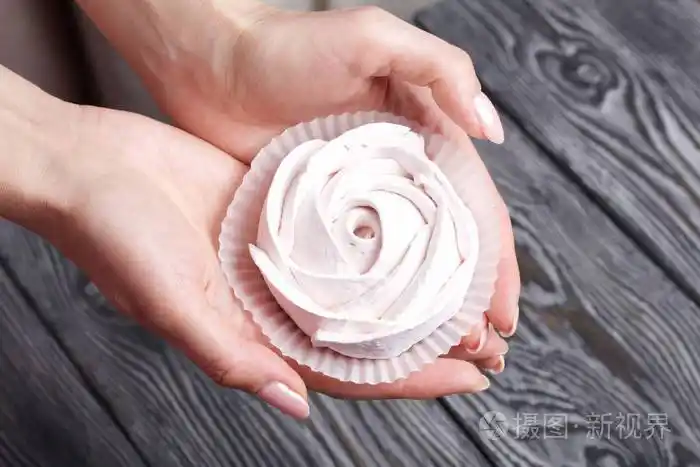 女人手掌中玫瑰状的棉花糖以黑白相间的拉丝松木板为背景