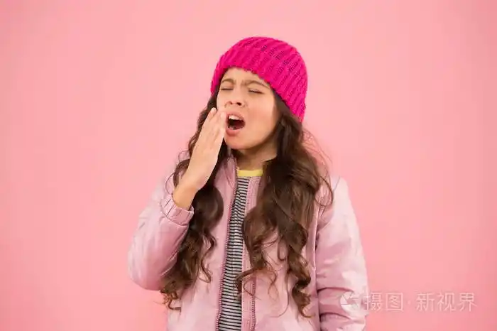 打喷嚏寒冷的气候小女孩生病了粉红色的背景儿童羽绒服和针织帽子冬季