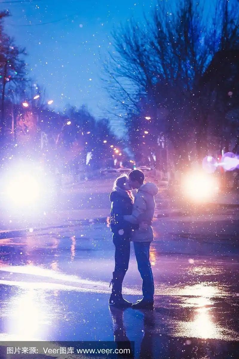 相爱的情侣在夜晚城市街道的雪中接吻.