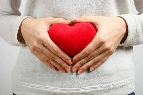 女人手里拿着红色的心在中立的背景上妊娠心脏病健康的概念