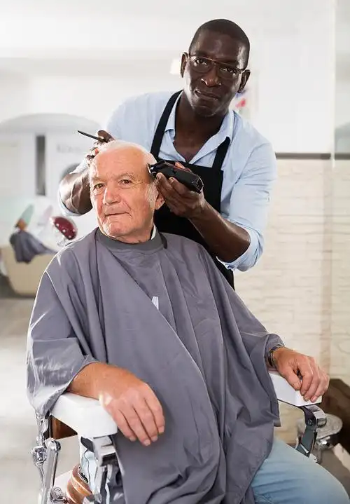 年长的男性客户正在接受非洲发型师的理发图片下载