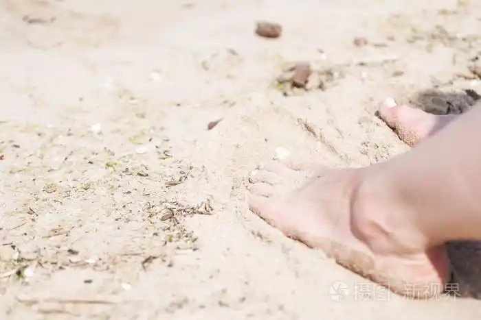 一个女人的脚与白色的钉子在海滩沙子在阳光下