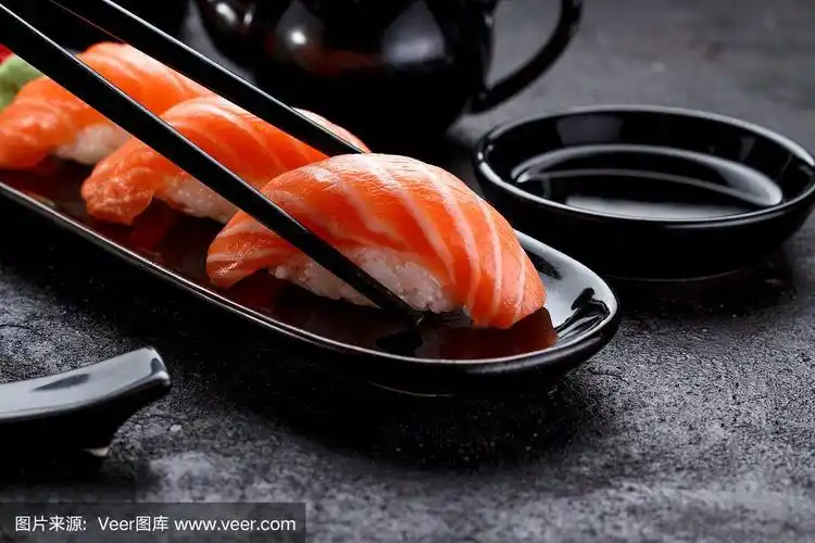 用筷子夹在黑色盘子里的三文鱼寿司手握寿司.