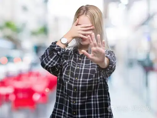 年轻的金发女人在孤立的背景上用手遮住眼睛,用悲伤和恐惧的表情做