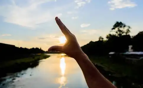 抓住最后一缕阳光.雄手指着太阳在蓝天上傍晚时分欣赏风景.