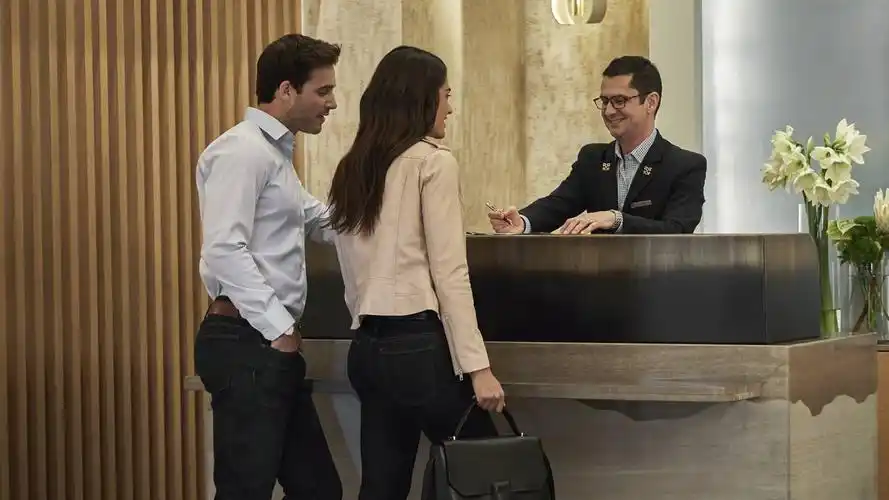 man and woman with tote bag stand at concierge desk with smiling
