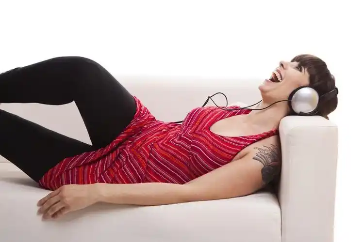 听音乐,美丽的女人躺在沙发和听音乐用耳机,白色上孤立