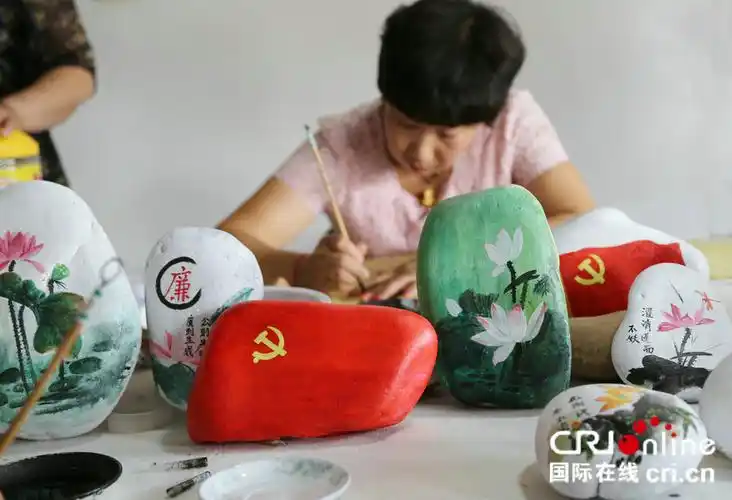 农民留守妇女在画师的指导下创作党旗廉政石头画