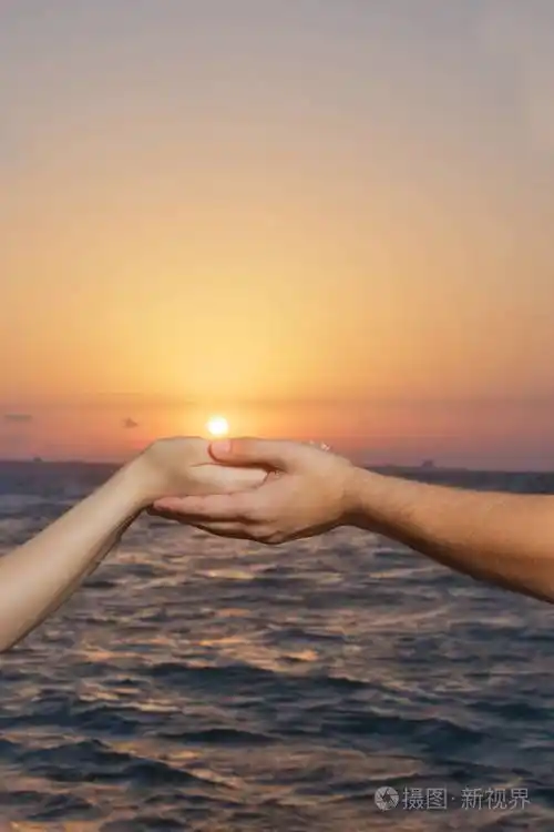 在太阳和天空的背景下牵手湖面上的手和太阳的手日落时的两只手他们