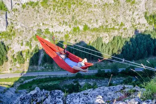 一个人在吊床上放松,吊床高高地搭在一根钢丝上,挂在离公路300米远的