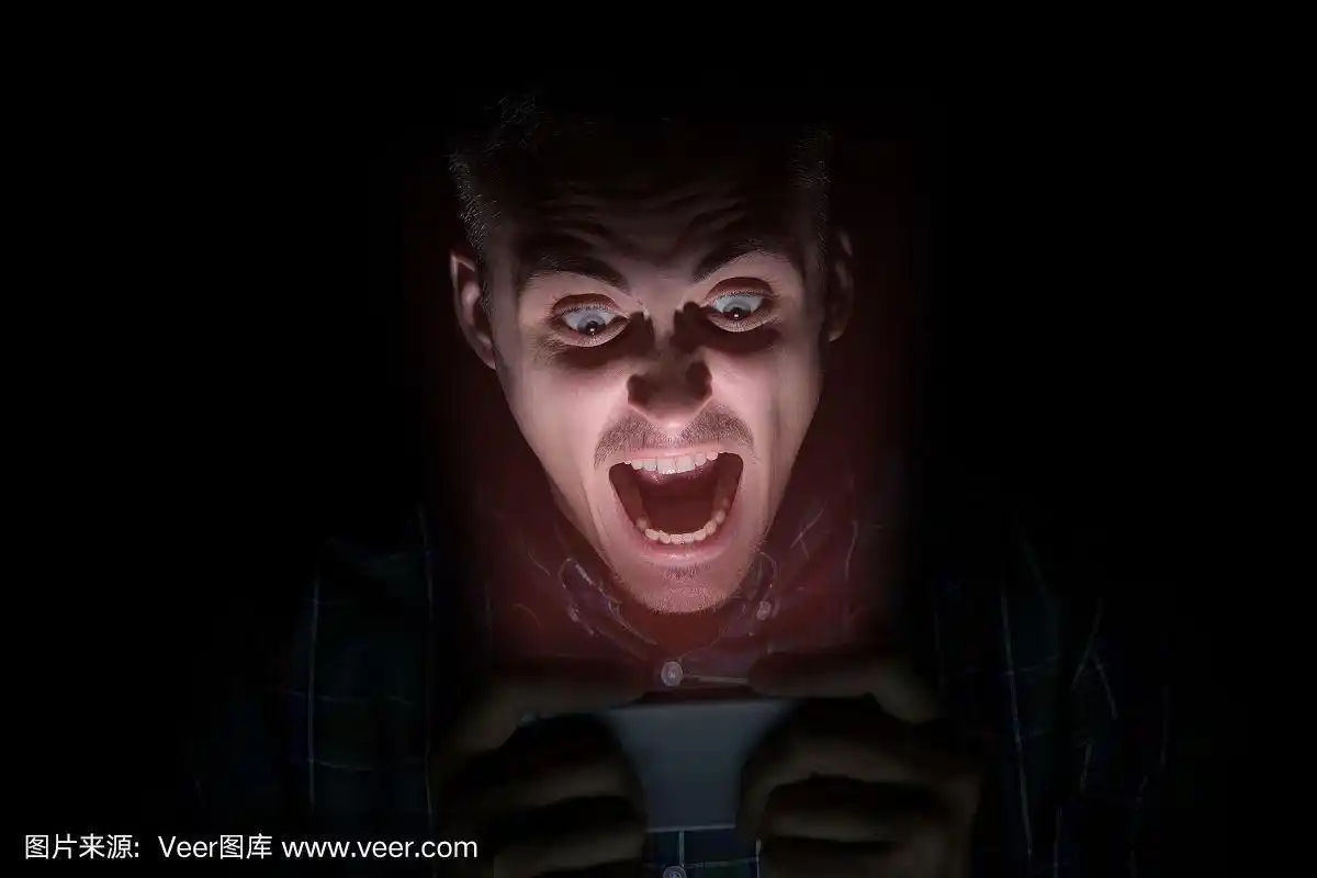 穿衬衫的人坐在黑暗中看手机.脸上是一种恐惧的情绪