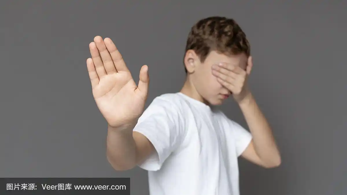 十几岁的男孩用手遮住眼睛,做着停止的手势