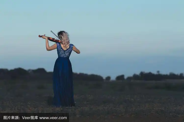 美丽的少女穿着长裙在田野里拉小提琴,少女的身影在自然的地平线上