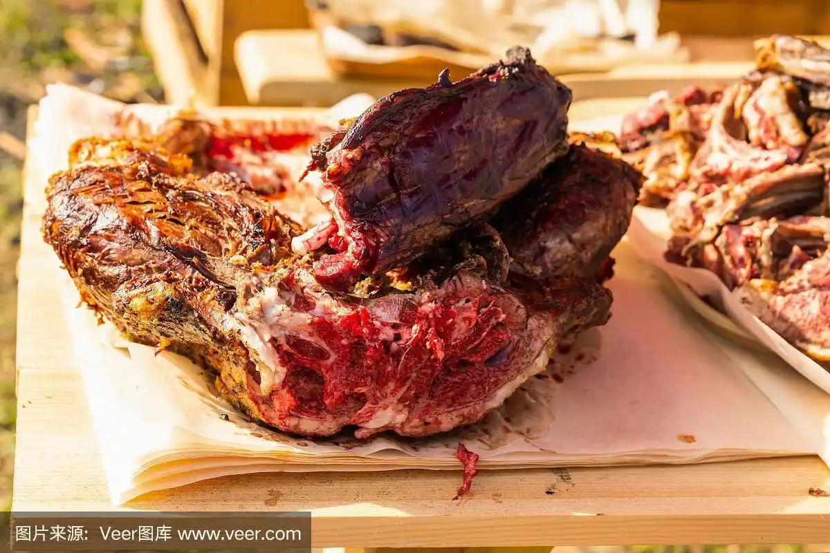 把大块的驼鹿肉切成薄片放在木桌上,放在烤架上烤