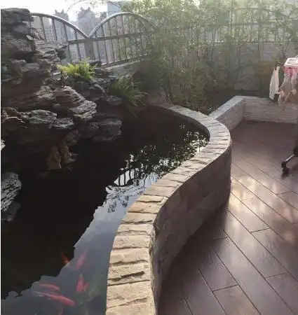 左侧是一个弧形的鱼池,内部设计假山花艺等作为点缀,搭配旁边的绿植后