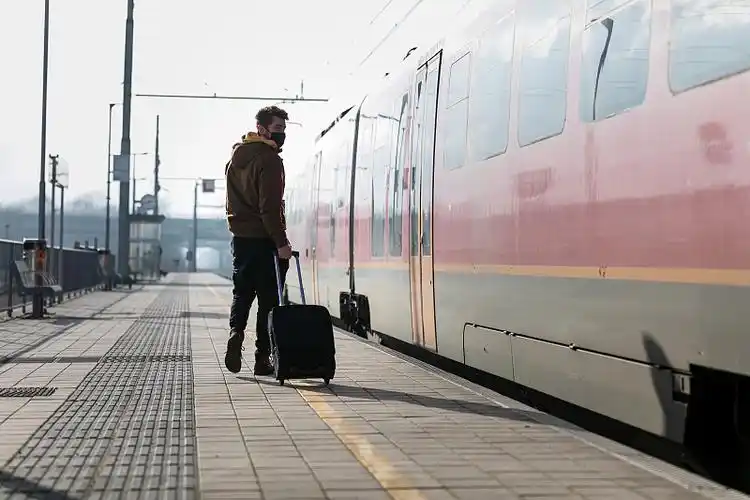 一个戴着防护面具,带着带轮子的行李箱的孤独男子在火车站等火车.