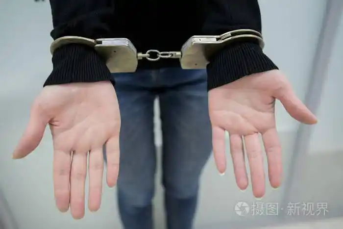 被逮捕的人用手铐将双手铐在灰色背景上背部.囚犯或被逮捕的手被铐.