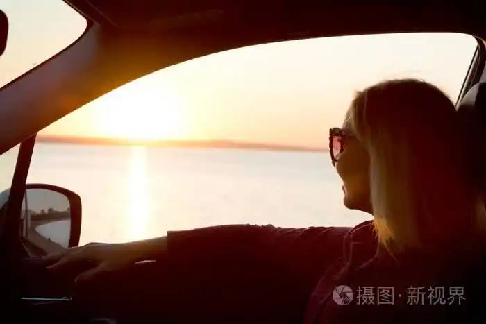 一名年轻女子看着窗外的车在日落的时候在海面上