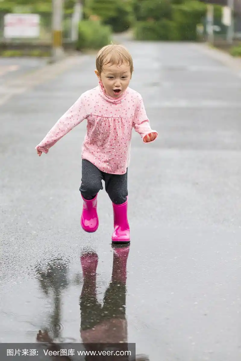 穿着雨靴的小女孩正要跑过水坑