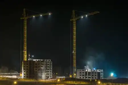 照明建筑工地夜间施工的塔式起重机和未完工的多层高层建筑照片