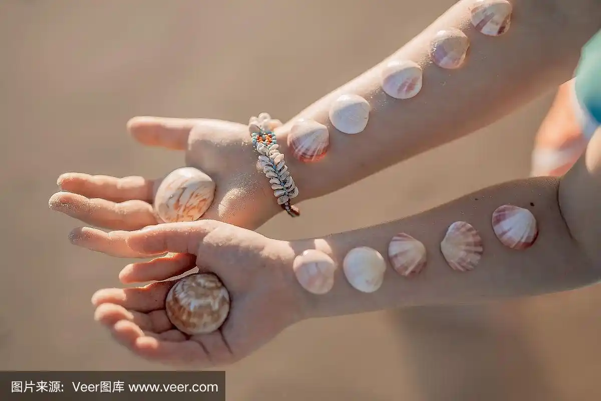 小女孩的手和贝壳在他们的海洋沙滩上的背景.