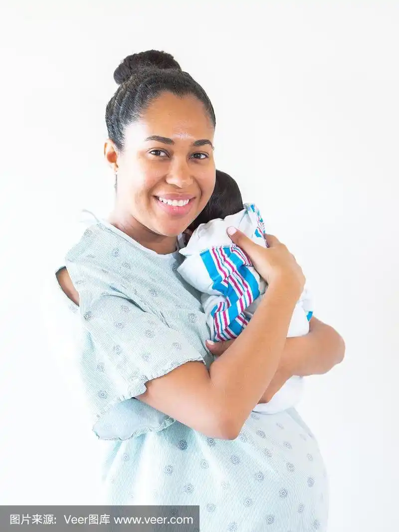 一位微笑的混血非洲裔美国母亲穿着病号服把她刚出生的婴儿搂在她的