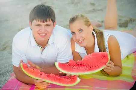西瓜一天快乐的情侣在野餐吃一个西瓜在沙滩上的白色衣服, 一个假日