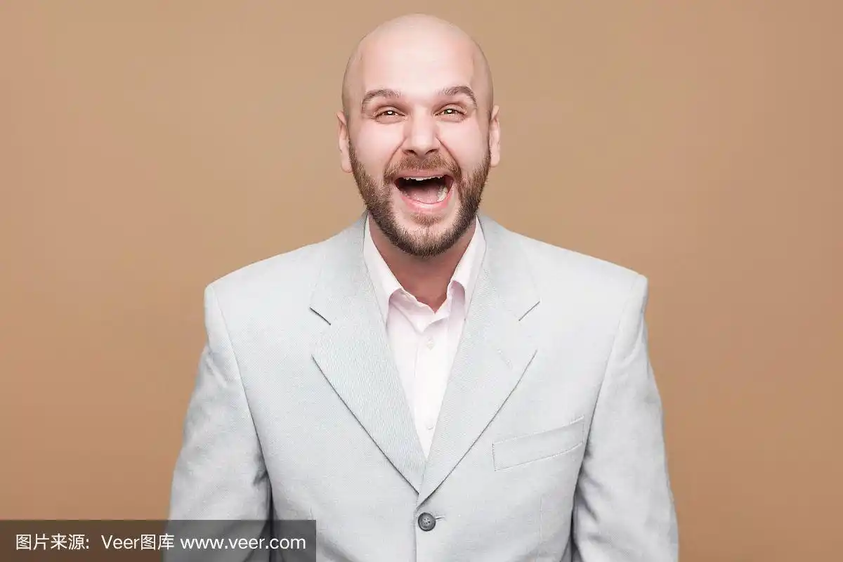 肖像快乐英俊的中年秃头胡子商人在经典的浅灰色西装站着,看着和笑的