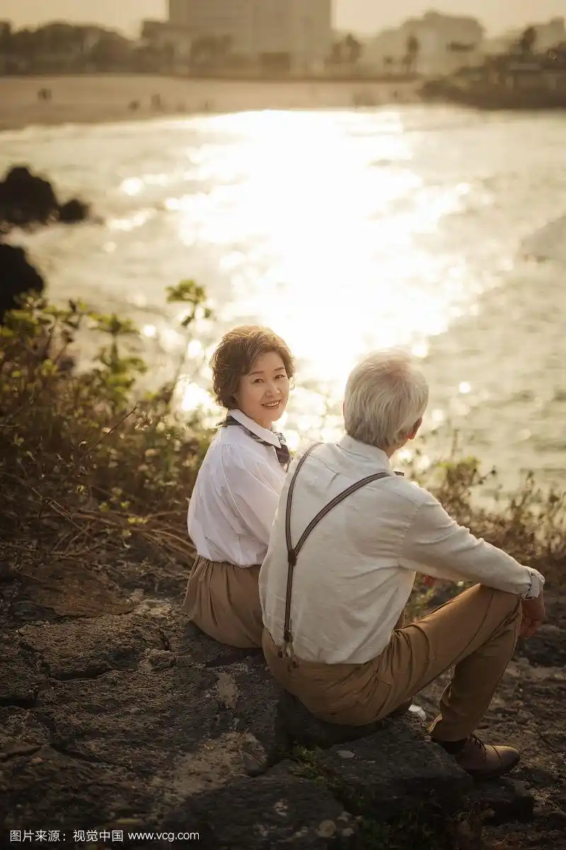 老年夫妇坐在地上看海滩景色的照片