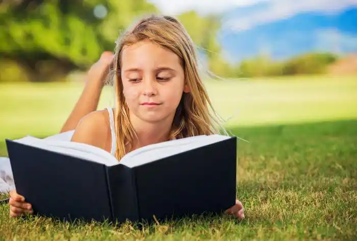 趴在草地上看书的外国小女孩图片