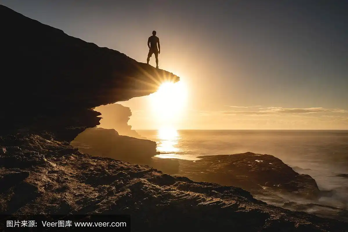 一个人的剪影站在海边的悬崖边看着忧郁的日落