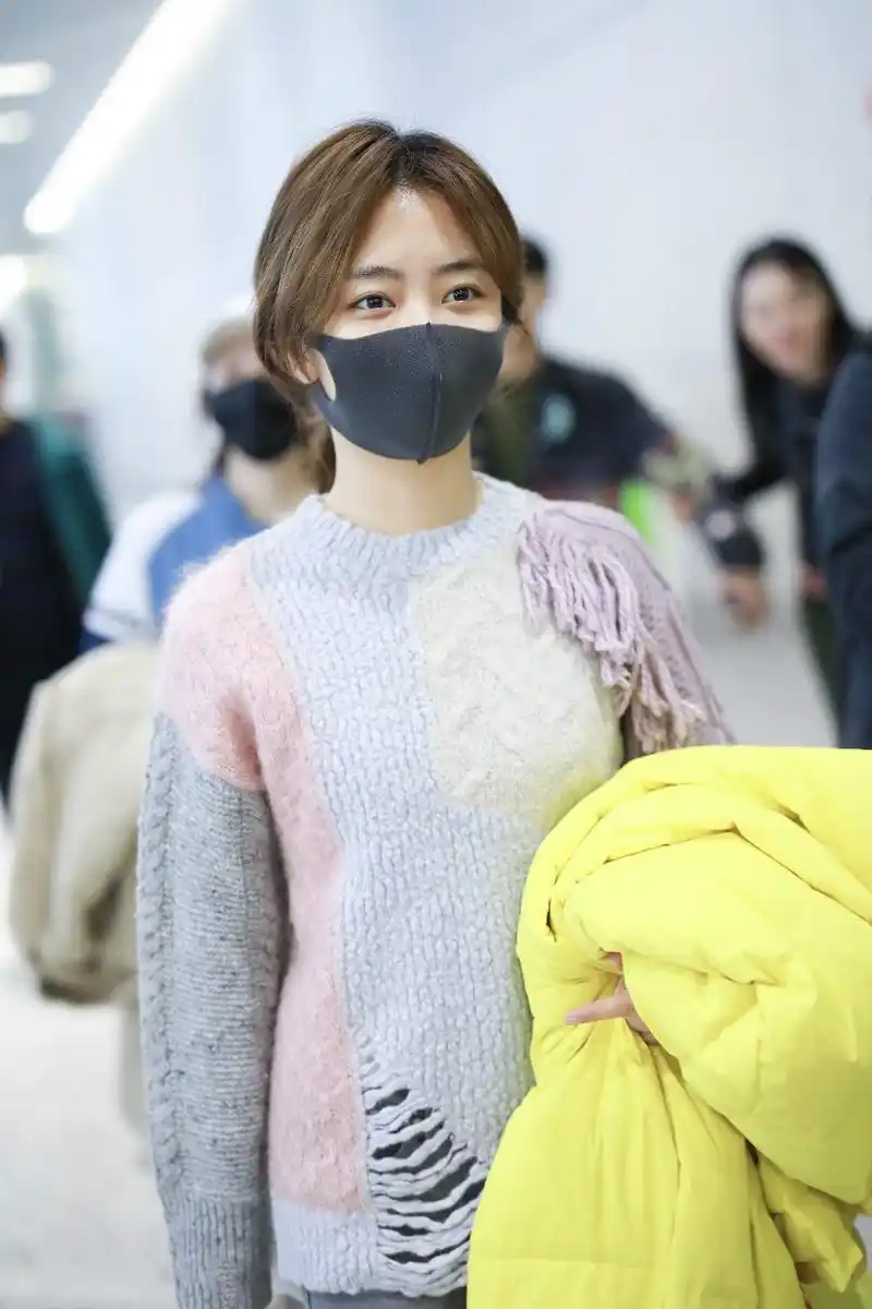 谭松韵戴口罩穿毛衣搭配牛仔裤现身机场,手里拿着黄色羽绒服
