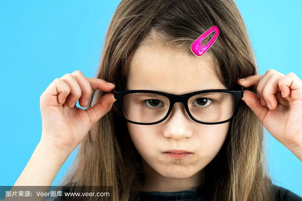 近距离的肖像愤怒的不高兴的孩子学校女孩戴眼镜孤立在蓝色的背景.